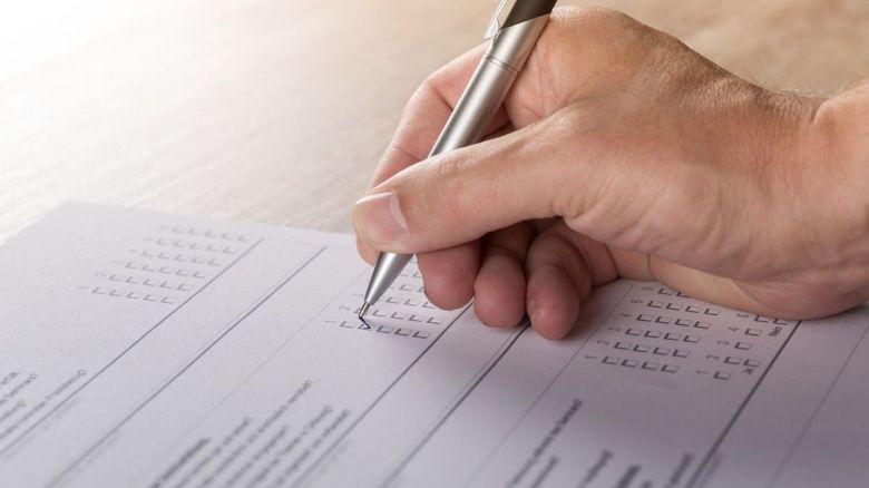 A white right hand fills out a tickbox questionnaire with a pen.