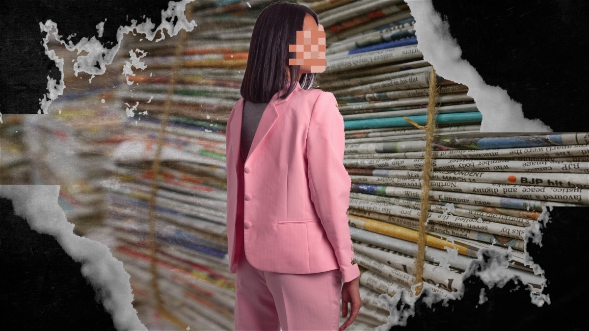 A woman in a pink suit and long black hair with her back to the camera, she turns her head to face the camera, but it is pixelated, behind her is a stack of newspapers.