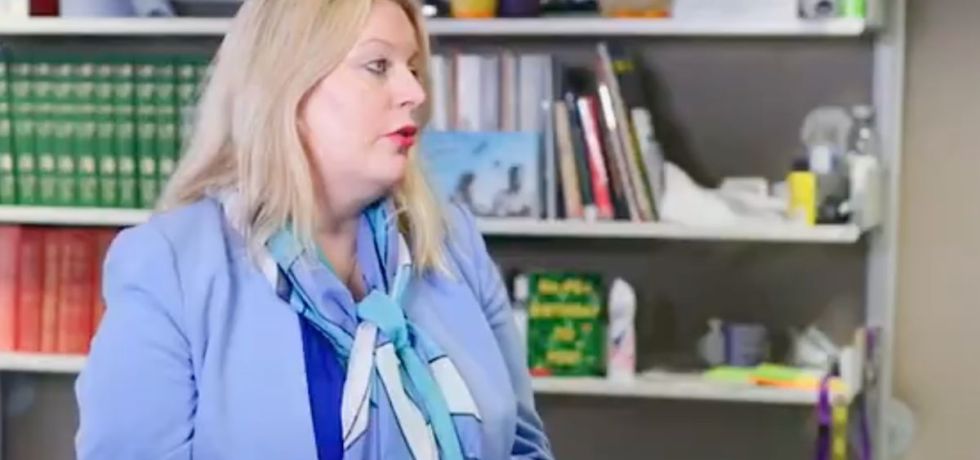 Mims Davies, a white woman with short blonde hair and a blue suit jacket, speaking to someone off-camera in her DWP office.
