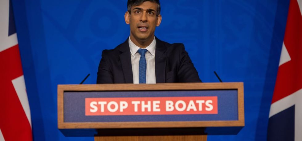 Rishi Sunak stands behind a wooden lectern with the text 'stop the boats' on it.